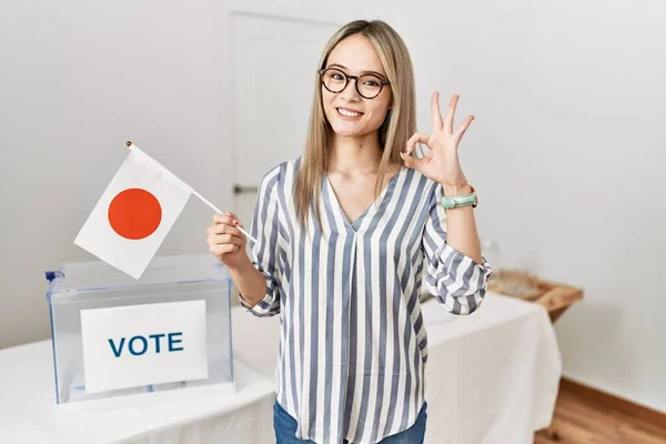 Asian young woman at political campaign election holding japan flag doing ok sign with fingers, smiling friendly gesturing excellent symbol