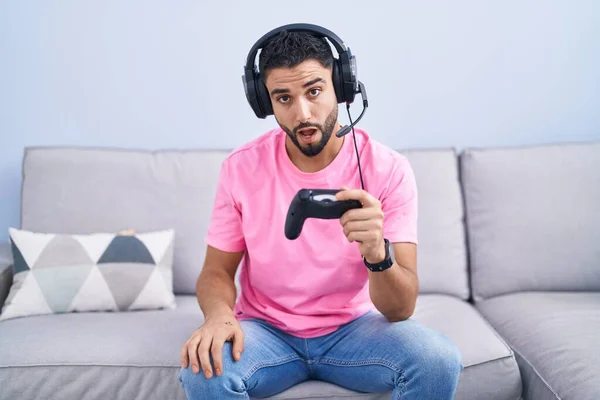 Hispanischer Junger Mann Der Videospiel Spielt Sitzt Mit Schockiertem Gesicht — Stockfoto