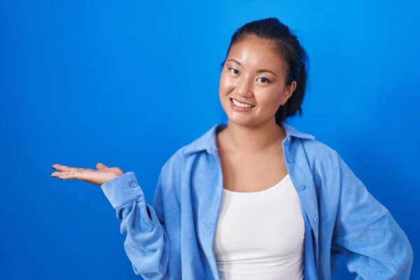 Asian Young Woman Standing Blue Background Smiling Cheerful Presenting Pointing — Stock Photo, Image