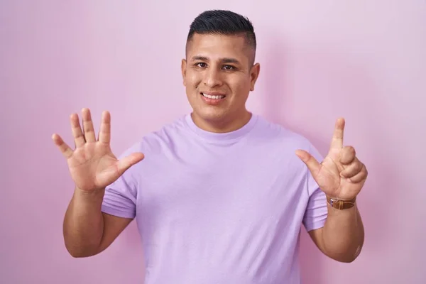 年轻的惊慌失措的男人站在粉红的背景上 用七号手指指指着 面带微笑 自信而快乐 — 图库照片