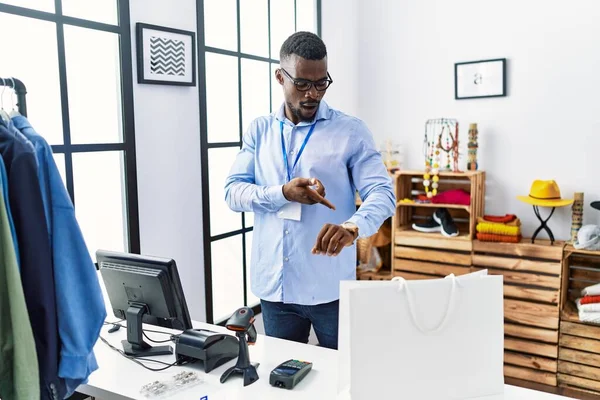 Young african man working as manager at retail boutique in hurry pointing to watch time, impatience, upset and angry for deadline delay