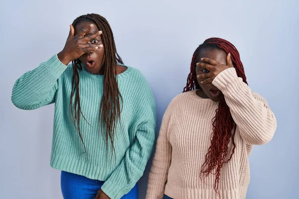 Две Африканки Стоящие Синем Фоне Заглядывая Лицо Глаза Закрывающие Лицо — стоковое фото