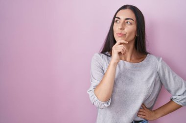 Pembe arka planda duran genç esmer kadın kameraya kollarını kavuşturup gülümseyerek ve çenesini kaldırarak bakıyor. Olumlu düşünmek. 