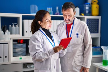 Orta yaşlı erkek ve kadın bilim adamları laboratuarda çalışan touchpad kullanıyorlar.