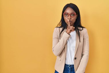 African young woman wearing glasses asking to be quiet with finger on lips. silence and secret concept. 