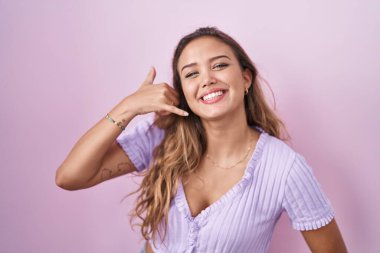 Pembe arka planda durup gülümseyen, el ve parmaklarıyla telefonla konuşan İspanyol bir kadın. iletişim kavramları. 