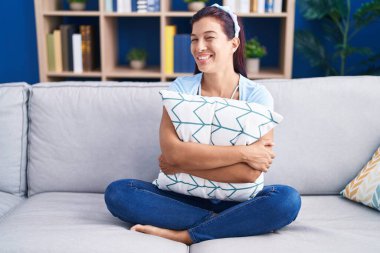 Kanepede oturmuş yastığı kucaklayan genç İspanyol kadın kameraya seksi bir ifadeyle bakıyor, neşeli ve mutlu bir yüzle.. 