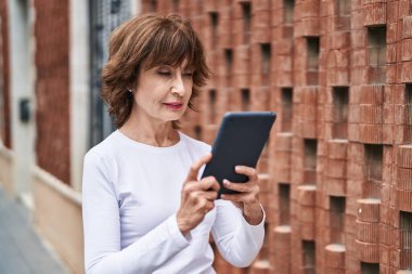 Orta yaşlı bir kadın sokakta ciddi bir ifadeyle dokunmatik ped kullanıyor.