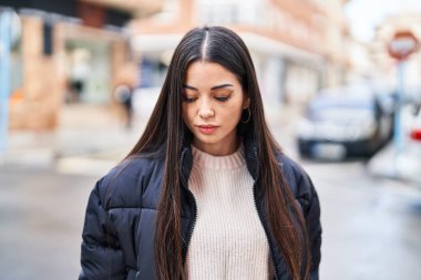 Young beautiful hispanic woman looking to the side with relaxed expression at street