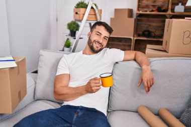 Genç İspanyol adam yeni evindeki kanepede kahve içiyor.
