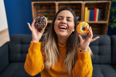 Genç İspanyol kadın evde donut yiyor, gülüyor ve kahkahalarla gülüyor.. 