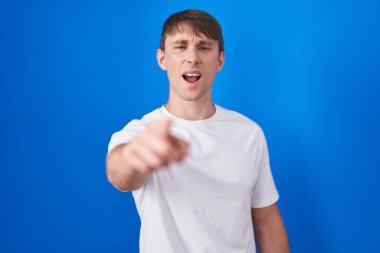 Caucasian blond man standing over blue background pointing displeased and frustrated to the camera, angry and furious with you 