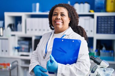 Afrikalı Amerikalı bilim kadını gülümsüyor. Laboratuvarda elinde bir pano var.