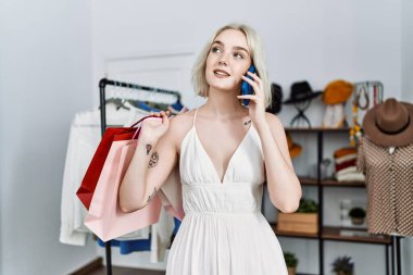Alışveriş torbaları tutan beyaz bir kadın giyim mağazasında akıllı telefondan konuşuyor.