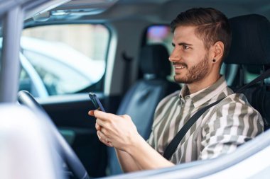 Beyaz bir adam akıllı telefon kullanıyor. Sokakta arabada oturuyor.