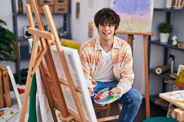 Genç İspanyol ressam, resim stüdyosunda kendine güvenen gülümsüyor.