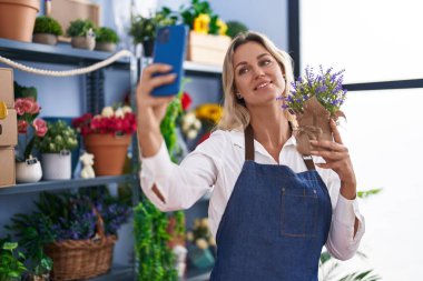 Young blonde woman florist make selfie by smartphone holding lavender plant at florist