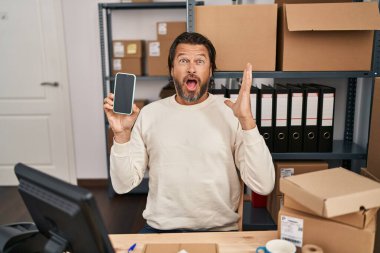 Küçük işletme şirketinde çalışan yakışıklı orta yaşlı bir adam elinde akıllı bir telefonla zaferi mutlu bir gülümsemeyle ve ellerini kaldırarak kazanan bir ifadeyle kutluyor. 