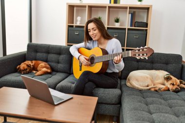 Latin kökenli genç bir kadının evde köpeklerle birlikte kanepede oturması.
