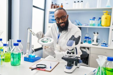 Genç Afrikalı Amerikalı adam bilim adamı üniforması giyiyor. Laboratuvarda Loupe 'u kullanıyor.