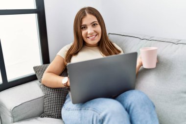 Genç İspanyol kadın evde kahve içerken dizüstü bilgisayar kullanıyor.