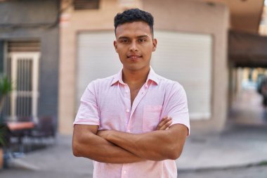 Young latin man smiling confident standing with arms crossed gesture at street