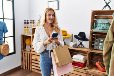 Young blonde woman using smartphone shopping at clothing store