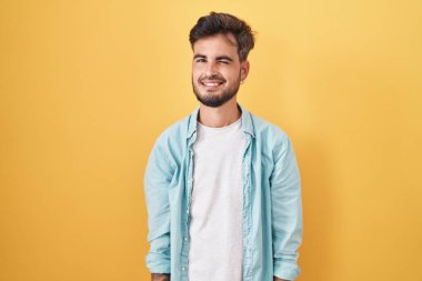 Young hispanic man with tattoos standing over yellow background winking looking at the camera with sexy expression, cheerful and happy face. 