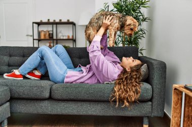 Genç, güzel, İspanyol bir kadın evdeki kanepede köpeğe sarılıyor.