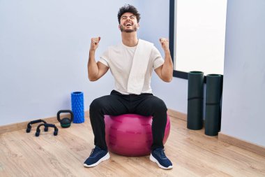 Sakallı İspanyol bir adam yoga odasında pilatese oturmuş kollarını kaldırarak ve açık gözlerle başarının şaşkınlığını ve şaşkınlığını yaşıyor. Kazanan konsept. 