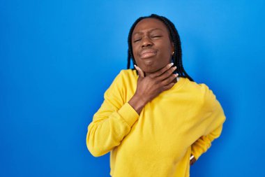 Beautiful black woman standing over blue background touching painful neck, sore throat for flu, clod and infection 