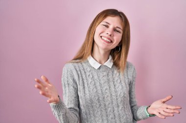 Güzel bir kadın pembe arka planda gülümsüyor. Kollarını açıp gülümsüyor. Hoş geldin, olumlu ve kendinden emin selamlar. 