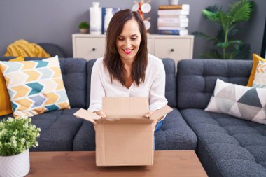 Middle age brunette woman opening cardboard box smiling with a happy and cool smile on face. showing teeth. 