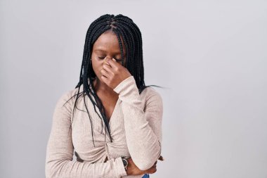 African woman with braids standing over white background tired rubbing nose and eyes feeling fatigue and headache. stress and frustration concept. 