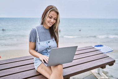 Genç beyaz kadın dışarıda bilgisayar kullanarak çalışıyor. Pozitif ve mutlu görünüyor. Kendine güvenen bir gülümsemeyle dişlerini gösteriyor. 