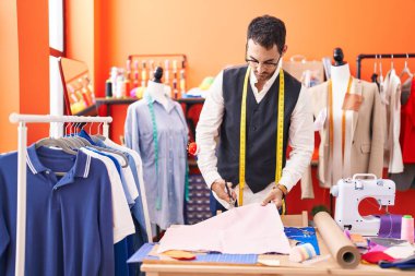 Young hispanic man tailor cutting cloth at atelier