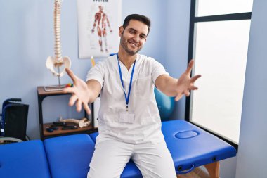 Ağrı kesici kliniğinde çalışan sakallı genç İspanyol adam kameraya sarılıp gülümsüyor. Mutluluğu kucaklayan neşeli bir ifade.. 