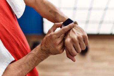 Young hispanic man wearing sportswear using stopwatch at sport center