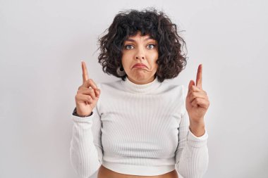 Kıvırcık saçlı İspanyol kadın izole edilmiş arka planda dikiliyor üzgün ve üzgün görünüyor, parmaklarıyla yönü gösteriyor, mutsuz ve depresif.. 