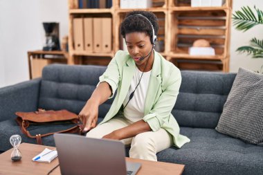Afrika kökenli Amerikalı bir kadın, danışma ofisinde kamerayı işaret ederek çevrimiçi oturum yapıyor. Kendine güvenen bir jest, ciddi görünüyor. 