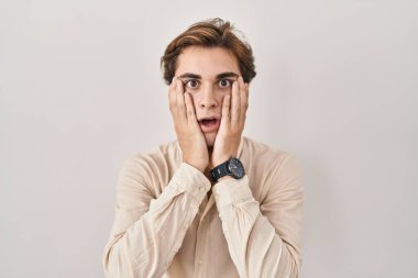 Young man standing over isolated background afraid and shocked, surprise and amazed expression with hands on face 