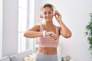 Young blonde woman listening to music using stopwatch at home