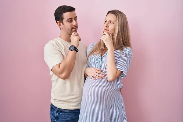 Young Couple Expecting Baby Standing Pink Background Hand Chin Thinking — Stock Photo, Image