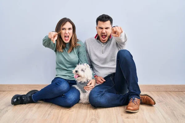 Young Hispanic Couple Sitting Floor Dog Pointing Displeased Frustrated Camera – stockfoto