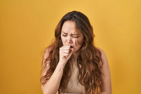 黄色の背景に立っている若いヒスパニック系の女性は気分が悪く 風邪や気管支炎の症状として咳をします ヘルスケアの概念 — ストック写真