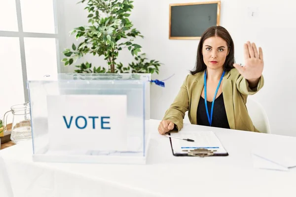 投票投票で選挙テーブルに座っている若いブルネットの女性は手の手のひらで歌うのをやめます 顔に負の重大なジェスチャーで — ストック写真