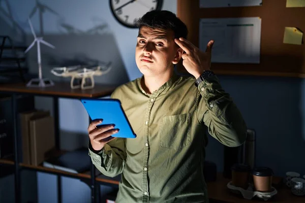 Non binary person using touchpad device at night shooting and killing oneself pointing hand and fingers to head like gun, suicide gesture.