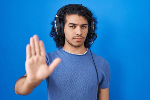 手の手のひらで歌うのをやめるヘッドフォンを使用して音楽を聞いて巻き毛を持つヒスパニック系の男 顔に負の重大なジェスチャーで — ストック写真