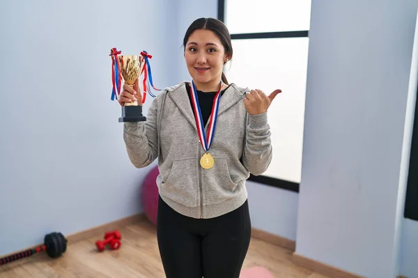 Young Latin Woman Holding Winner Trophy Pointing Thumb Side Smiling — Stockfoto