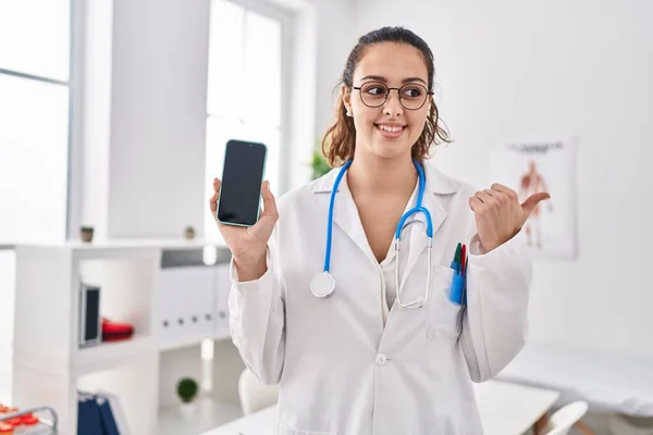 Young Hispanic Doctor Woman Holding Smartphone Showing Screen Pointing Thumb — Stock Photo, Image